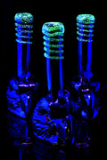 UV-lit glass bong trio with metallic eagle bases and bright green glow-in-the-dark frit neck rings