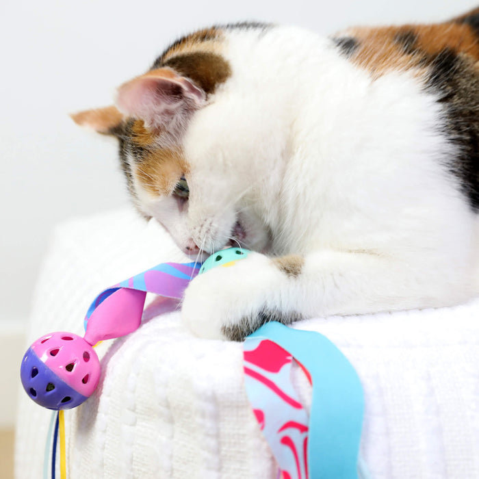 A calico cat plays with Quirky Kitty Catnip Seaweed Tumblers, ocean-themed toys infused with catnip, while lying on a white textured surface.