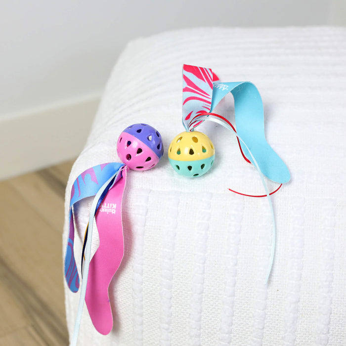 Two Quirky Kitty Catnip Seaweed Tumblers sit on a white textured surface near a light wood floor and wall. These ocean-themed cat toys come in a 2-pack and feature colorful plastic balls, ribbons, and catnip.