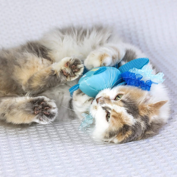 A fluffy calico cat lies on a white textured surface, playfully snuggling the Quirky Kitty Octopurr Kicker – an ocean-themed catnip kicker toy with ribbon accents from Quirky Kitty.