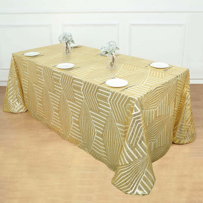 Gold leaf patterned tablecloth draped over a table with plates and vases.